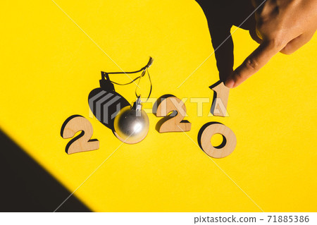 Wooden numbers 2021 chainging 2020 with child hand and a silver christmas ball on a yellow background. 71885386