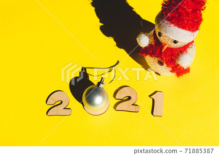 Wooden numbers 2021, snowman and a silver christmas ball on a yellow background. 71885387