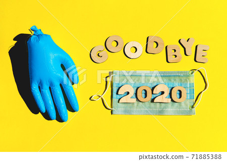 Words GOODBYE 2020 from wooden letters on a yellow background, inflated medical glove and facemask. 2020 and epidemic concept. 71885388