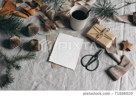 Christmas greeting card mockup. Cup of coffee, paper Christmas ornaments and gift box. Velvet ribbons, pine tree branches. Linen table cloth background. Vintage moody winter still life. Festive table. Christmas greeting card mockup. Cup of coffee, paper Christmas ornaments and gift box. Velvet ribbons, pine tree branches. Linen table cloth background. Vintage moody winter still life. Festive table. 71886020