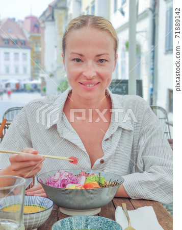 Woman eating tasty colorful healthy natural organic vegetarian Hawaiian poke bowl using asian chopsticks on rustic wooden table. Healthy natural organic eating concept Woman eating tasty colorful healthy natural organic vegetarian Hawaiian poke bowl using asian chopsticks on rustic wooden table. Healthy natural organic eating concept 71889142
