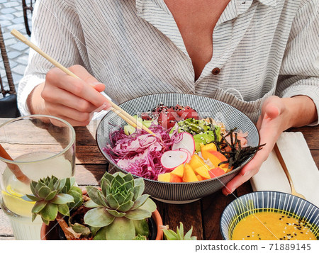 Woman eating tasty colorful healthy natural organic vegetarian Hawaiian poke bowl using asian chopsticks on rustic wooden table. Healthy natural organic eating concept Woman eating tasty colorful healthy natural organic vegetarian Hawaiian poke bowl using asian chopsticks on rustic wooden table. Healthy natural organic eating concept 71889145