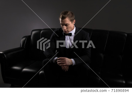Elegant man sitting on sofa and checking time 71890894