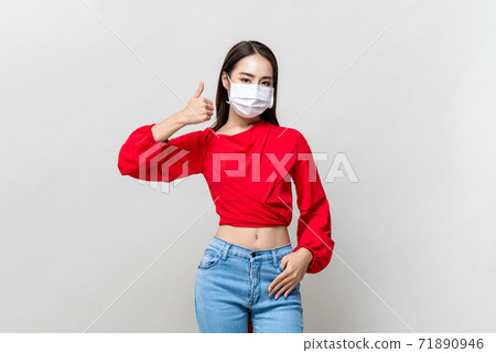 Young Asian woman wearing face mask to protect COVID-19 and giving thumbs up 71890946