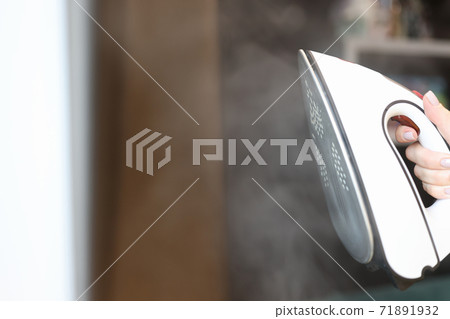 Woman holding iron with steamer in her hands closeup 71891932
