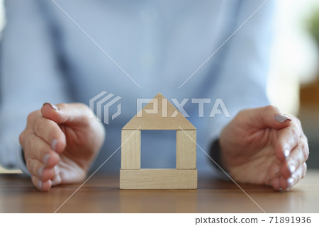 Woman covering wooden house with her hand closeup 71891936