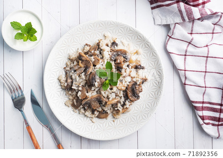Risotto with mushrooms on a white plate. Boiled white rice with champignons in cream sauce. Light wooden background. Copy space 71892356