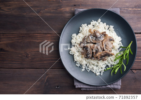 Risotto with mushrooms on a black plate. Boiled white rice with champignons in cream sauce. Dark wooden background. Copy space Risotto with mushrooms on a black plate. Boiled white rice with champignons in cream sauce. Dark wooden background. Copy space 71892357