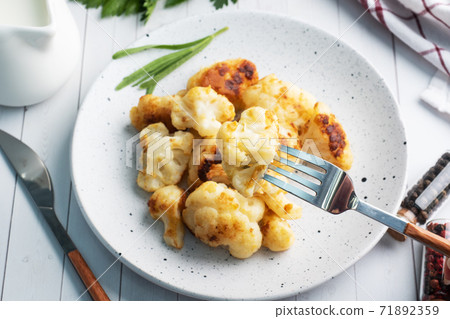 Fried cauliflower florets in batter on a white plate. White wooden background. Fried cauliflower florets in batter on a white plate. White wooden background. 71892359