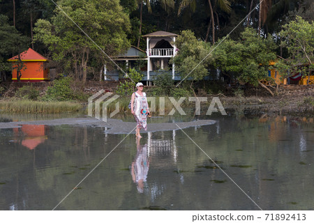 Barefoot woman enters the water of the lagoon near the village in the jungle in Goa, India 71892413