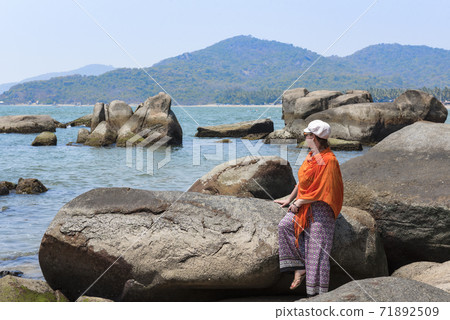A young woman with an orange handkerchief admires the view of the rocky coast of the Indian ocean A young woman with an orange handkerchief admires the view of the rocky coast of the Indian ocean 71892509