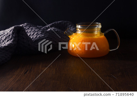 Hot tea with sea buckthorn in a glass pot on the dark wooden table. 71895640