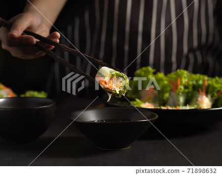 Female cook gripping  Vietnamese spring rolls with chopstick in dark background 71898632