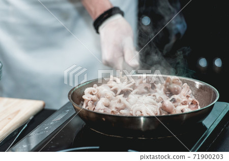 The chef cooks the small octopus on a metal frying pan 71900203