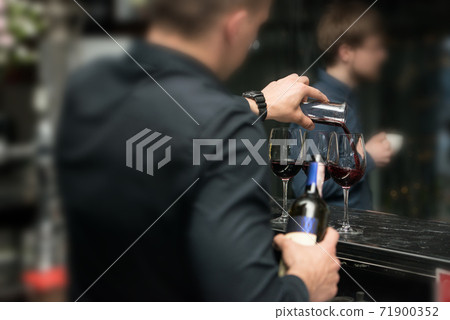 Barman pouring red wine into glasses in detail 71900352
