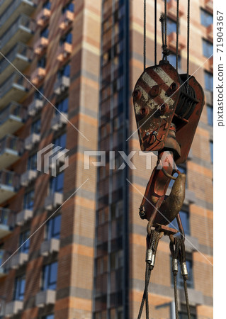 Construction crane hook with multi-storey building under construction (new residential complex) on the background. Construction site upon renovation program in Cheryomushki district, Moscow, Russia Construction crane hook with multi-storey building under construction (new residential complex) on the background. Construction site upon renovation program in Cheryomushki district, Moscow, Russia 71904367