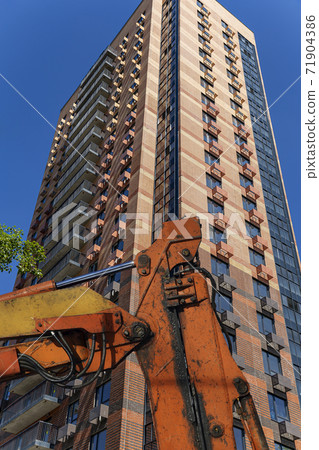 Part of a construction machine (excavator or crane) with multi-storey building under construction (new residential complex) on the background. Construction site upon renovation program in Cheryomushki 71904386