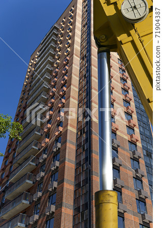 Part of a construction machine (excavator or crane) with multi-storey building under construction (new residential complex) on the background, Moscow, Russia Part of a construction machine (excavator or crane) with multi-storey building under construction (new residential complex) on the background, Moscow, Russia 71904387