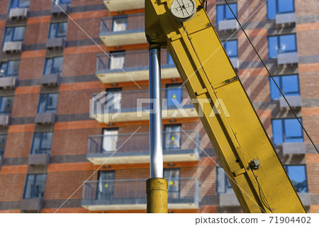 Part of a construction machine (excavator or crane) with multi-storey building under construction (new residential complex) on the background, Moscow, Russia Part of a construction machine (excavator or crane) with multi-storey building under construction (new residential complex) on the background, Moscow, Russia 71904402