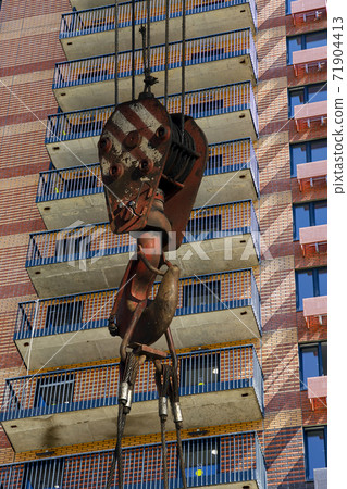 Construction crane hook with multi-storey building under construction (new residential complex) on the background. Construction site upon renovation program in Cheryomushki district, Moscow, Russia Construction crane hook with multi-storey building under construction (new residential complex) on the background. Construction site upon renovation program in Cheryomushki district, Moscow, Russia 71904413