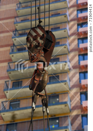 Construction crane hook with multi-storey building under construction (new residential complex) on the background. Construction site upon renovation program in Cheryomushki district, Moscow, Russia Construction crane hook with multi-storey building under construction (new residential complex) on the background. Construction site upon renovation program in Cheryomushki district, Moscow, Russia 71904414