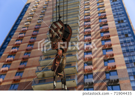 Construction crane hook with multi-storey building under construction (new residential complex) on the background. Construction site upon renovation program in Cheryomushki district, Moscow, Russia Construction crane hook with multi-storey building under construction (new residential complex) on the background. Construction site upon renovation program in Cheryomushki district, Moscow, Russia 71904435