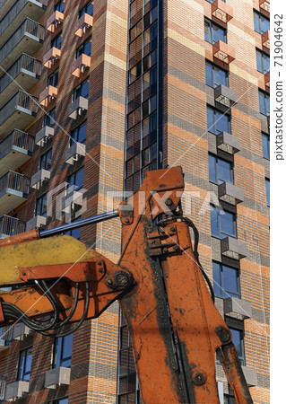 Part of a construction machine with multi-storey building under construction (new residential complex) on the background. Part of a construction machine with multi-storey building under construction (new residential complex) on the background. 71904642