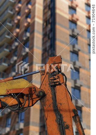 Part of a construction machine with multi-storey building under construction (new residential complex) on the background. Part of a construction machine with multi-storey building under construction (new residential complex) on the background. 71904648