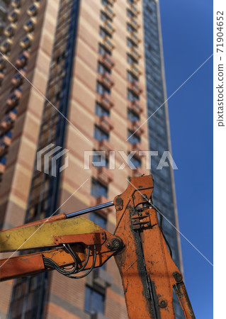 Part of a construction machine with multi-storey building under construction (new residential complex) on the background. Part of a construction machine with multi-storey building under construction (new residential complex) on the background. 71904652