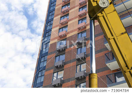 Part of a construction machine (excavator or crane) with multi-storey building under construction (new residential complex) on the background, Moscow, Russia Part of a construction machine (excavator or crane) with multi-storey building under construction (new residential complex) on the background, Moscow, Russia 71904784