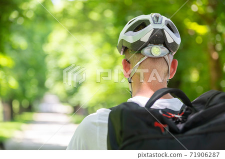 Rear view of unrecognizable man wearing protective helmet on bicycle cycling in city park 71906287