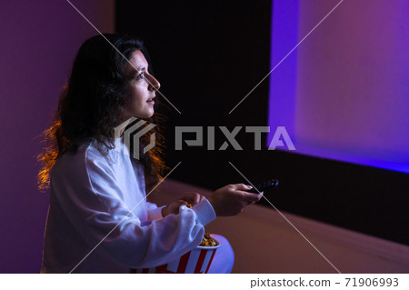 person watches a movie sitting on the couch with a bucket of popcorn 71906993