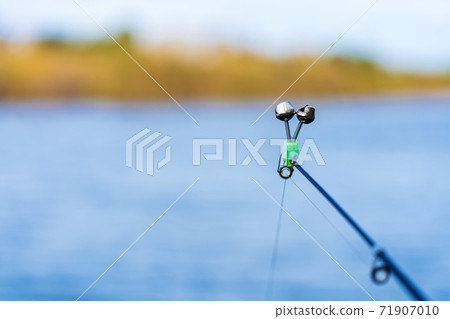 Fishing rod with a bell on the background of the river. Fishing hobby Fishing rod with a bell on the background of the river. Fishing hobby 71907010