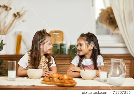 little children girls having breakfast - fresh delicious croissants and milk 71907295