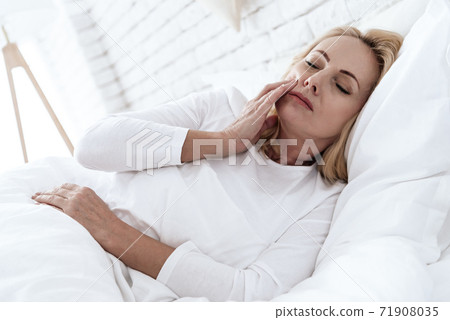 Woman in white bed with severe pain in her teeth. Woman in white bed with severe pain in her teeth. 71908035