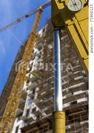 Part of a construction machine (excavator or crane) with multi-storey building under construction with scaffolding (new residential complex) on the background, Moscow, Russia 71908123