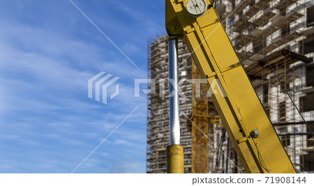 Part of a construction machine (excavator or crane) with multi-storey building under construction with scaffolding (new residential complex) on the background, Moscow, Russia 71908144