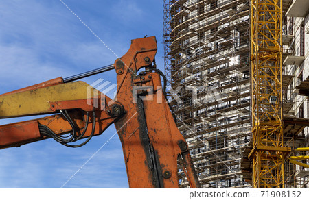 Part of a construction machine (excavator or crane) with multi-storey building under construction with scaffolding (new residential complex) on the background, Moscow, Russia 71908152