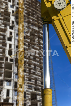 Part of a construction machine (excavator or crane) with multi-storey building under construction with scaffolding (new residential complex) on the background, Moscow, Russia 71909071
