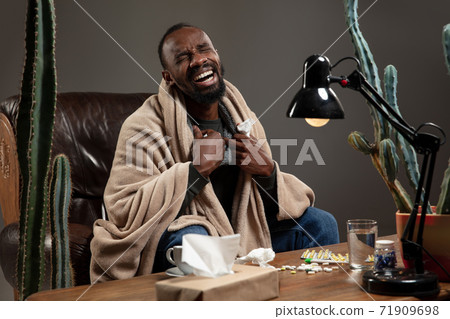 Young African-american man wrapped in a plaid looks sick, ill, sitting at home indoors. Healthcare concept 71909698
