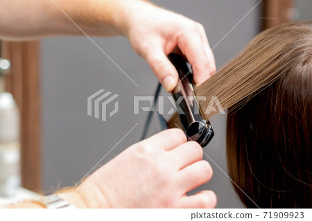 Hairdresser straightens hair of woman. 71909923
