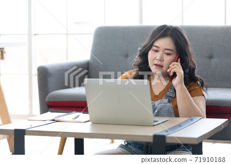 chubby woman typing on laptop computer and talking on the phone for work or study 71910188