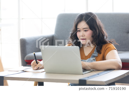 chubby woman looking at laptop computer and writing on notebook for work or study 71910190