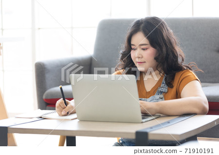 chubby woman looking at laptop computer and writing on notebook for work or study 71910191