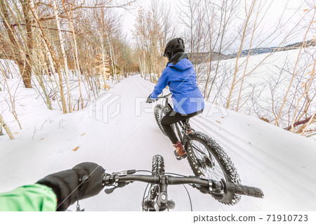 Couple biking on fat bikes on winter snow trail outdoor. Mountain nature landscape, woman rider cycling from behind with point of view of man holding handlebar of his bike 71910723