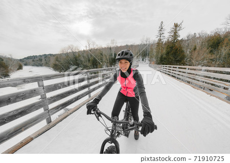 Winter bike sport fun happy cyclist Asian girl cycling on snow bridge with fat e-bike. Electric biking 71910725