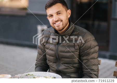 Handsome man sitting outdoors in cafe on terrace and smiled to camera 71911229