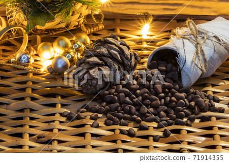 Cone and pine nuts on the braided surface. Christmas tree and lights. Cone and pine nuts on the braided surface. Christmas tree and lights. 71914355