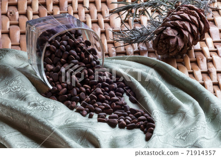 Cone and pine nuts in the glass on the braided surface and green napkin Cone and pine nuts in the glass on the braided surface and green napkin 71914357
