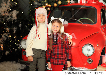 Children on the background of a red car with New Year's gifts. 71919798